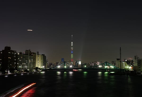 Naechtliche Stadtansicht am Wasser mit Bruecke, Lichtspuren und beleuchtetem Turm