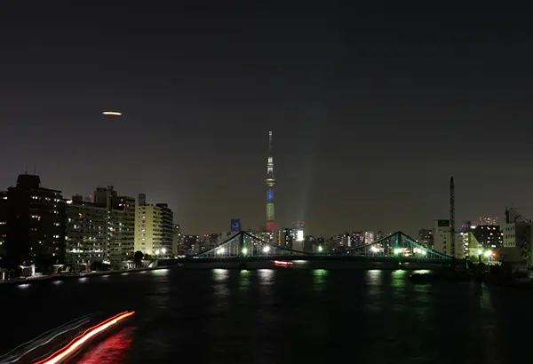 Naechtliche Stadtansicht am Wasser mit Bruecke, Lichtspuren und beleuchtetem Turm