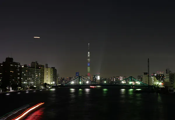 Naechtliche Stadtansicht am Wasser mit Bruecke, Lichtspuren und beleuchtetem Turm
